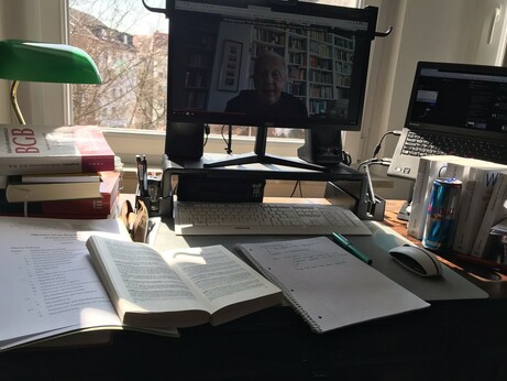 Foto von meinem Schreibtisch. Ein aufgeschlagenes BGB, ein Vorlesungsskript, Bücherstapel, Block mit handschriftlichen Notizen, ein Füller, Computerbildschirm auf dem eine Person vor einer Bücherwand zu sehen ist. Rechts im Foto ein Thinkpad, eine Dose Redbull, Gesetzesbücher.