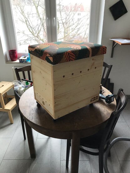 Die fertige Wurmkiste. Eine Kiste aus Holz mit Löchern zum Atmen, bzw. als Belüftung. Auf der Oberseite befindet sich ein Poster, die Kiste ist als Hocker verwendbar.