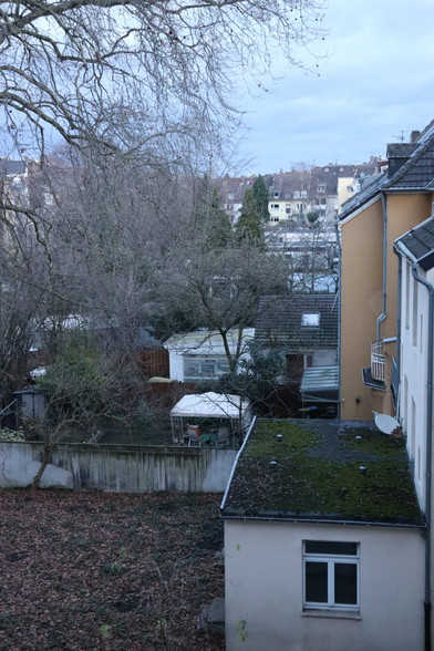 Foto aus meinem Badezimmerfenster auf die Hinterhöfe in der Nachbarschaft. Aufgenommen im Winter, die Bäume sind kahl, es liegt teils noch Laub auf dem Boden. Manche Gärten sind kultiviert, andere eher wild.